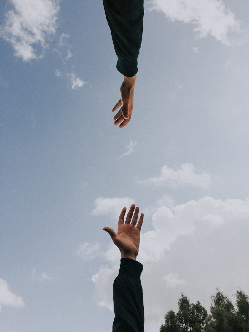 Twee handen die elkaar bijna raken tegen een lucht met wolken
